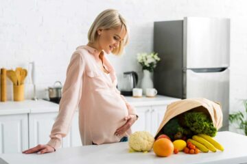Jeune femme enceinte avec un panier de légumes bio sur ordonnances vertes