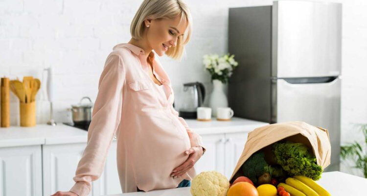 Jeune femme enceinte avec un panier de légumes bio sur ordonnances vertes